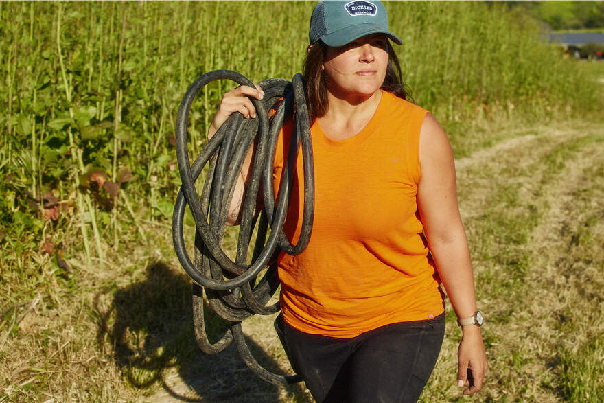 Woman in orange sleeveless carrying garden hose